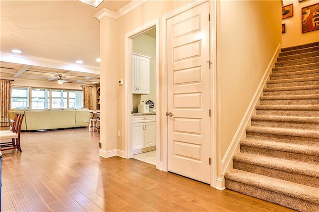 staircase featuring coffered ceiling, ceiling fan, ornamental molding, beamed ceiling, and wood-type flooring