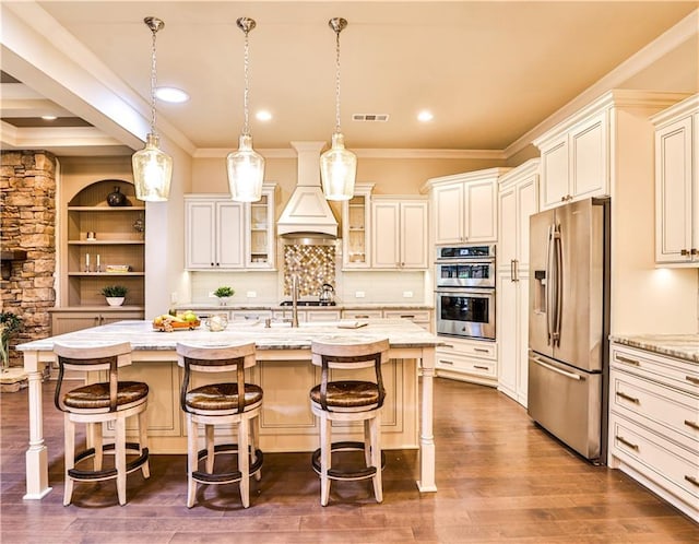 kitchen with stainless steel appliances, pendant lighting, a breakfast bar area, a kitchen island with sink, and custom range hood