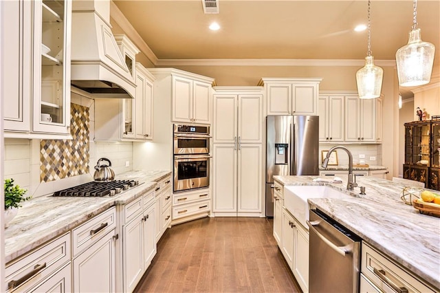 kitchen with appliances with stainless steel finishes, tasteful backsplash, custom range hood, sink, and decorative light fixtures