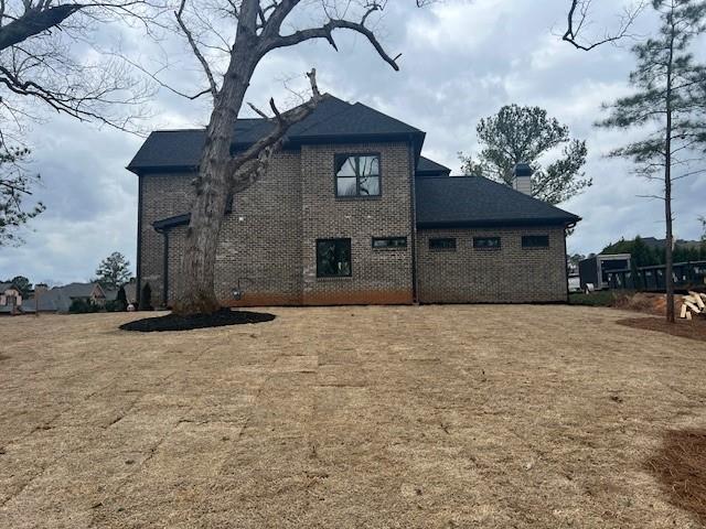 back of house featuring brick siding, a yard, and a chimney