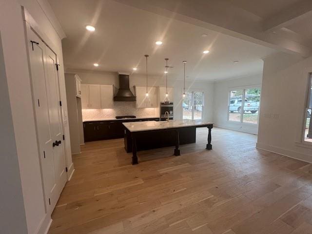 kitchen with light wood finished floors, cooktop, light countertops, custom range hood, and a kitchen island with sink