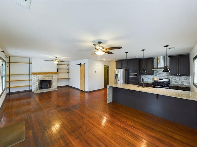 kitchen featuring a barn door, appliances with stainless steel finishes, light stone countertops, wall chimney range hood, and a breakfast bar area