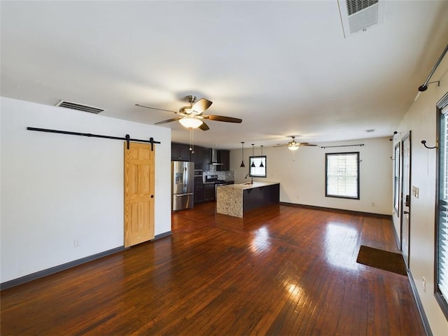 unfurnished living room with a barn door, ceiling fan, and dark hardwood / wood-style floors