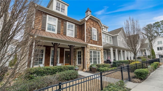 view of front of home featuring a fenced front yard, a porch, a standing seam roof, metal roof, and stone siding