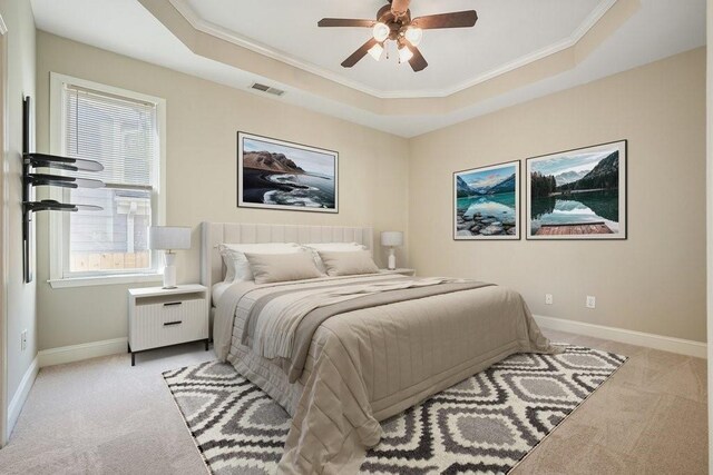 bedroom with ornamental molding, ceiling fan, a raised ceiling, and light colored carpet