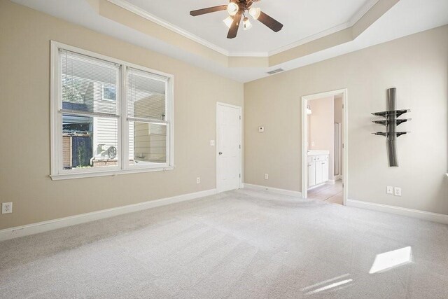 empty room featuring ceiling fan, a raised ceiling, ornamental molding, and light carpet