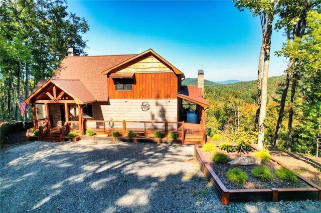 chalet / cabin featuring covered porch, a chimney, and a view of trees