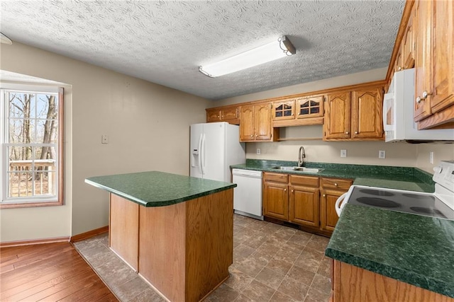 kitchen with a sink, dark countertops, a center island, white appliances, and baseboards