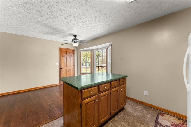 kitchen featuring dark countertops, a kitchen island, baseboards, ceiling fan, and brown cabinets