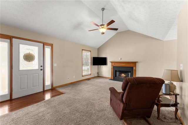 living room featuring a ceiling fan, baseboards, lofted ceiling, a fireplace with flush hearth, and a textured ceiling