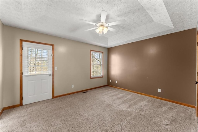 carpeted empty room featuring a tray ceiling, baseboards, a textured ceiling, and a ceiling fan