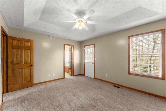 unfurnished bedroom featuring visible vents, multiple windows, a tray ceiling, and carpet floors