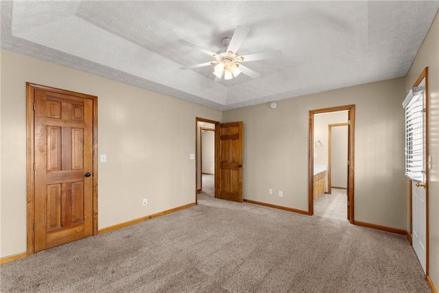 unfurnished bedroom featuring light carpet, a ceiling fan, a tray ceiling, a textured ceiling, and baseboards