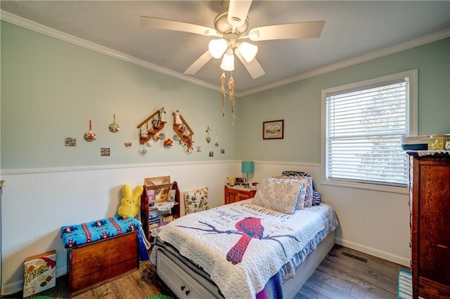 bedroom with a wainscoted wall, visible vents, ornamental molding, and wood finished floors