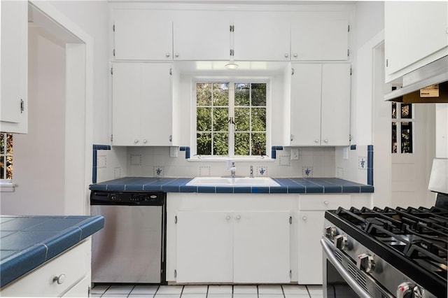 kitchen with appliances with stainless steel finishes, tile countertops, tasteful backsplash, white cabinetry, and sink