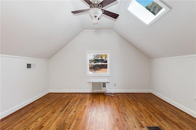 bonus room featuring hardwood / wood-style floors, an AC wall unit, vaulted ceiling with skylight, and ceiling fan