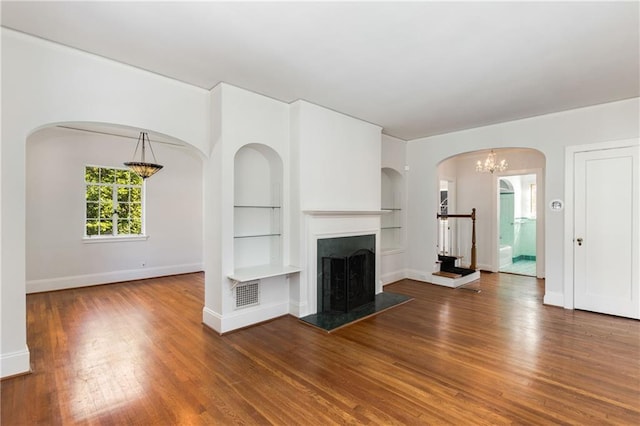 unfurnished living room with wood-type flooring, built in features, and a chandelier