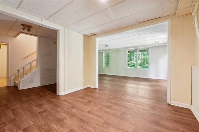 spare room with a paneled ceiling, stairway, baseboards, and wood finished floors