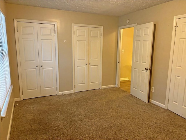 unfurnished bedroom featuring a textured ceiling, multiple closets, multiple windows, and carpet floors