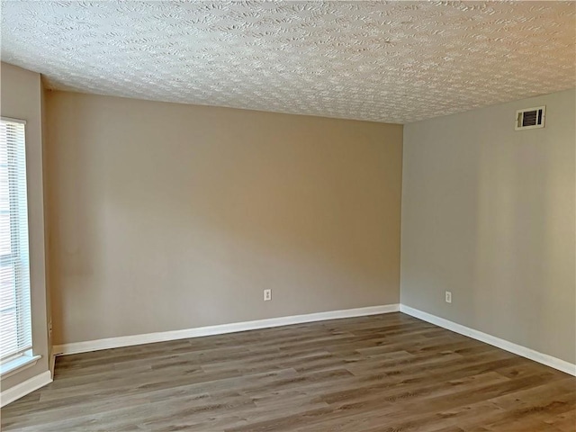 spare room featuring dark hardwood / wood-style floors, a textured ceiling, and plenty of natural light