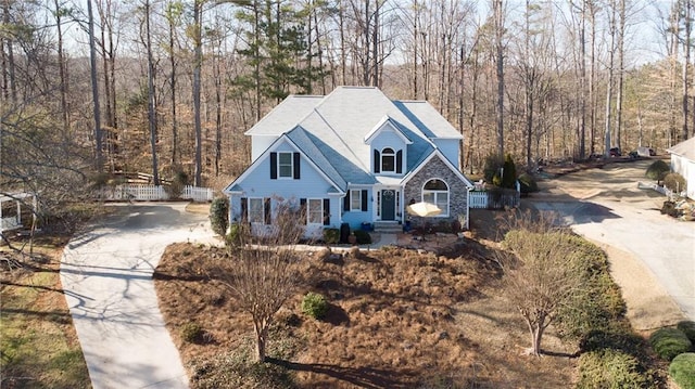 view of front of home with stone siding, a forest view, fence, and driveway