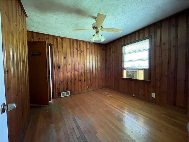 empty room featuring visible vents, hardwood / wood-style floors, a textured ceiling, cooling unit, and a ceiling fan