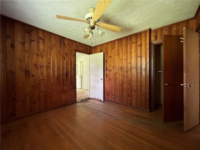 unfurnished room featuring wooden walls, a textured ceiling, ceiling fan, and wood finished floors
