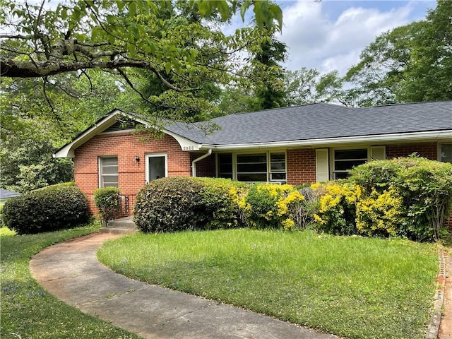 ranch-style home with brick siding, a shingled roof, and a front lawn