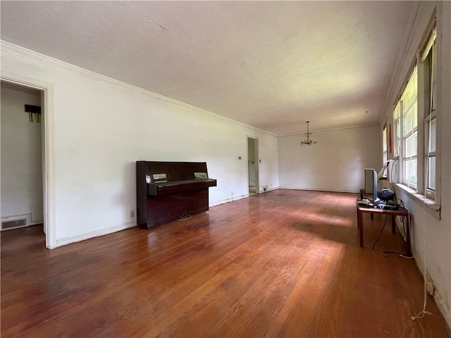unfurnished living room featuring visible vents, ornamental molding, wood finished floors, and a chandelier