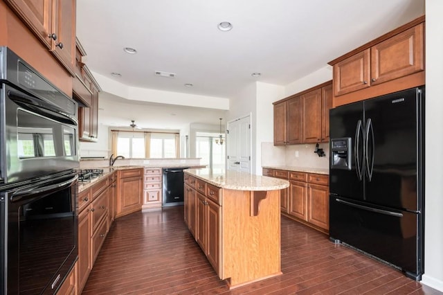kitchen featuring visible vents, light stone counters, black appliances, a peninsula, and dark wood-type flooring