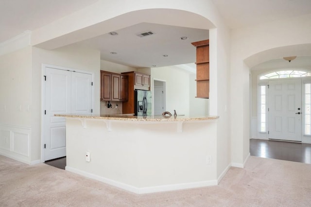 kitchen featuring carpet flooring, arched walkways, a kitchen breakfast bar, stainless steel refrigerator with ice dispenser, and visible vents
