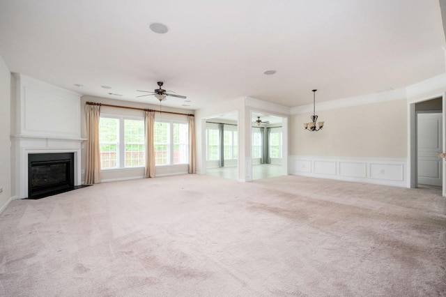 unfurnished living room featuring carpet, a fireplace with flush hearth, ceiling fan with notable chandelier, and a decorative wall