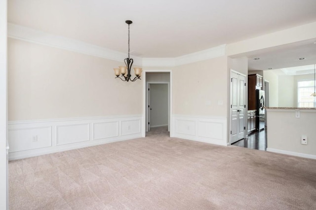 spare room featuring carpet floors, a decorative wall, an inviting chandelier, and a wainscoted wall
