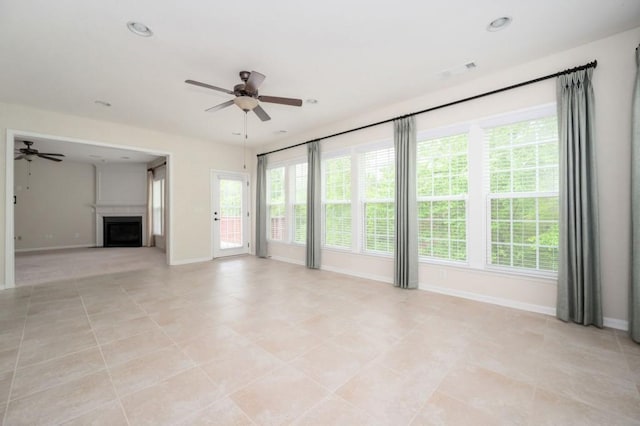 unfurnished living room with ceiling fan, a wealth of natural light, and baseboards