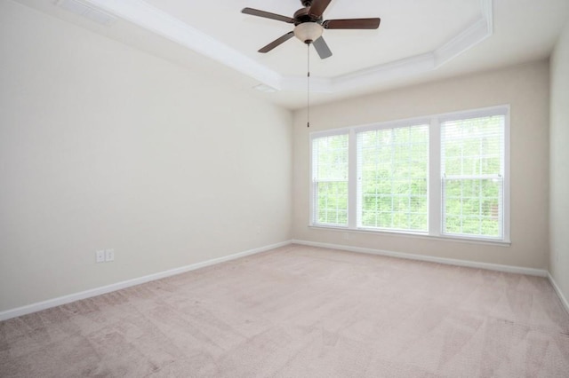 empty room featuring a ceiling fan, ornamental molding, baseboards, a raised ceiling, and carpet flooring