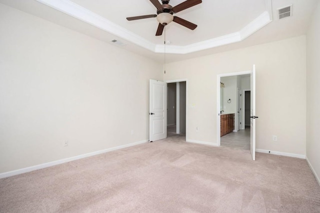 unfurnished bedroom with light colored carpet, baseboards, visible vents, and a raised ceiling