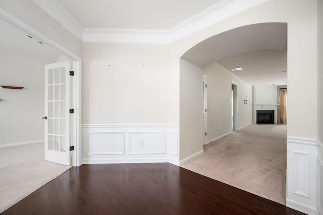 carpeted empty room with crown molding, arched walkways, hardwood / wood-style flooring, and a fireplace