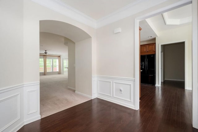 empty room featuring crown molding, arched walkways, wood-type flooring, and a wainscoted wall