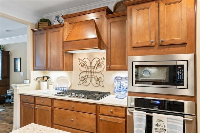 kitchen featuring stainless steel appliances, brown cabinets, premium range hood, backsplash, and crown molding
