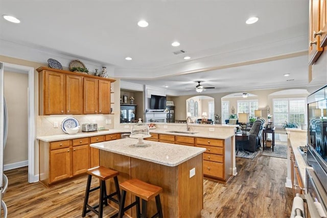 kitchen featuring open floor plan, a peninsula, a sink, a ceiling fan, and wood finished floors