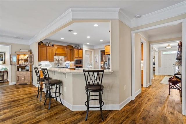 kitchen featuring appliances with stainless steel finishes, crown molding, a kitchen breakfast bar, dark wood-type flooring, and brown cabinets