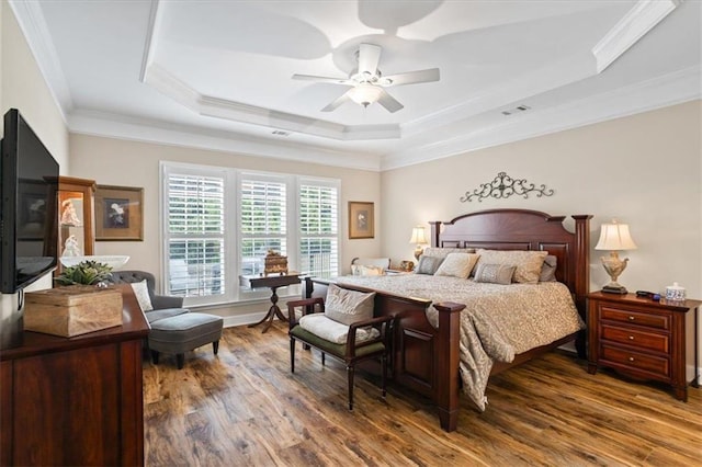 bedroom with a raised ceiling, wood finished floors, ornamental molding, and a ceiling fan