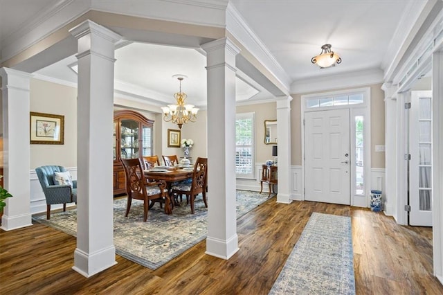 foyer featuring decorative columns, dark wood finished floors, wainscoting, a chandelier, and ornamental molding