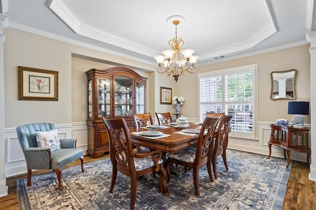 dining space featuring a chandelier, wood finished floors, a tray ceiling, crown molding, and wainscoting