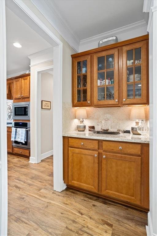 bar area featuring stainless steel appliances, tasteful backsplash, light wood-style floors, crown molding, and baseboards