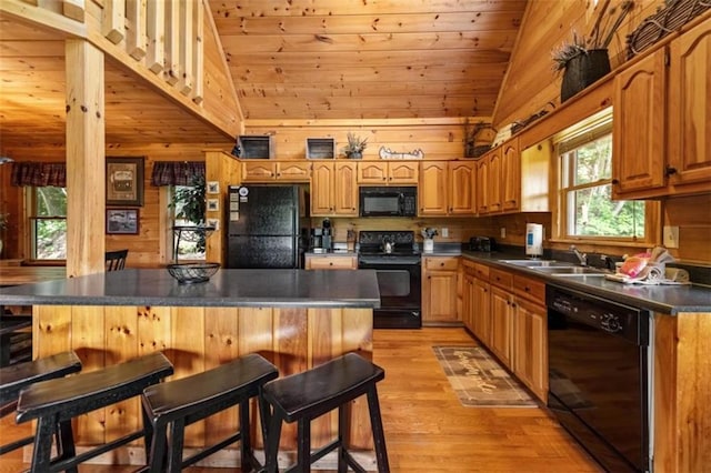 kitchen featuring wood walls, a sink, light wood-type flooring, black appliances, and a breakfast bar area