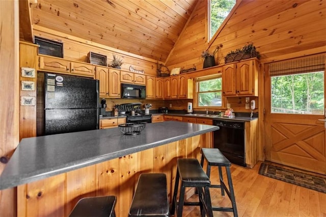 kitchen featuring dark countertops, a sink, black appliances, light wood-style floors, and a breakfast bar