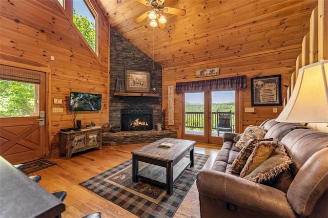 living area featuring high vaulted ceiling, a ceiling fan, a stone fireplace, wood finished floors, and wood walls