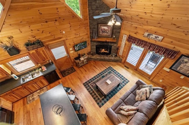 living room featuring high vaulted ceiling, a stone fireplace, a healthy amount of sunlight, and wood finished floors