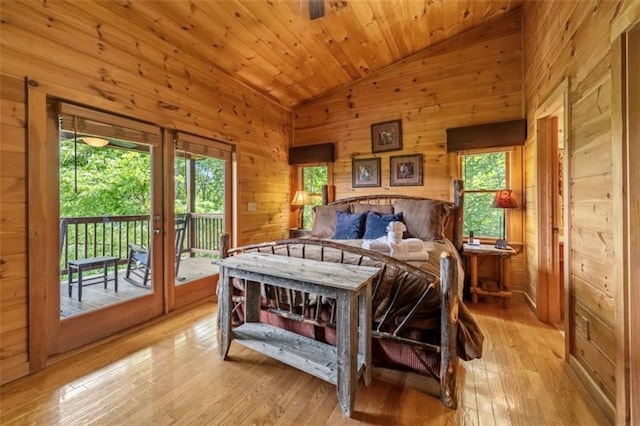 bedroom featuring vaulted ceiling, multiple windows, wooden walls, and access to exterior